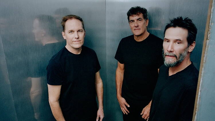 Wide shot of three band members posing together in a metallic room.