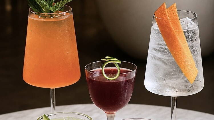 Close-up of three colorful cocktails garnished with fruit and herbs on a tabletop. Close-up of three colorful cocktails garnished with fruit and herbs on a tabletop.
