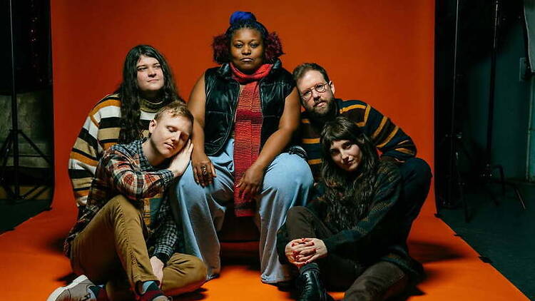 Group portrait of five band members posing on an orange studio backdrop. Group portrait of five band members posing on an orange studio backdrop.