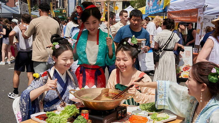 Wide shot of people in traditional attire sharing a hot pot meal at an outdoor street festival. Wide shot of people in traditional attire sharing a hot pot meal at an outdoor street festival.