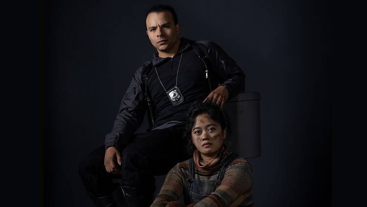 Portrait of two performers in costume posing against a dark studio backdrop.