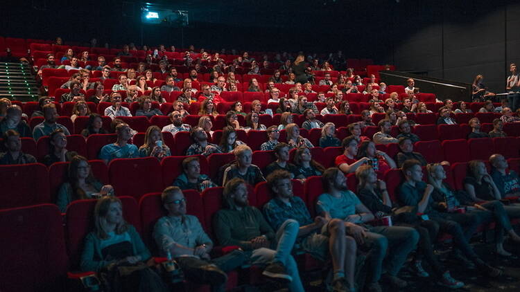 A wide shot of an audience watching a film in a movie theater. A wide shot of an audience watching a film in a movie theater.