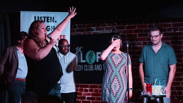 A wide shot of performers entertaining an audience on a comedy club stage. A wide shot of performers entertaining an audience on a comedy club stage.