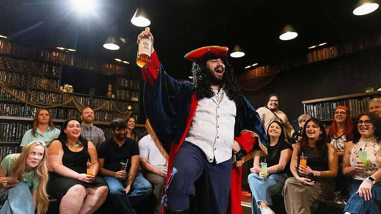 A wide shot of a costumed performer entertaining an audience in a themed venue. A wide shot of a costumed performer entertaining an audience in a themed venue.