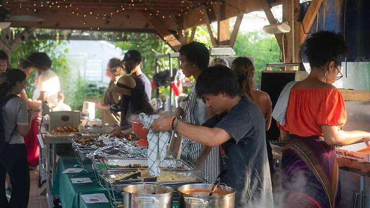 A wide shot of people serving food at an outdoor community gathering. A wide shot of people serving food at an outdoor community gathering.