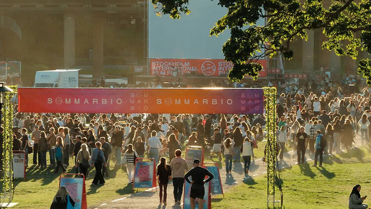 Stockholm film festival, open air movie every august, Rålis A large crowd gathered on a sunny park lawn under a banner for Sommarbio, the outdoor cinema event hosted by the Stockholm International Film Festival.