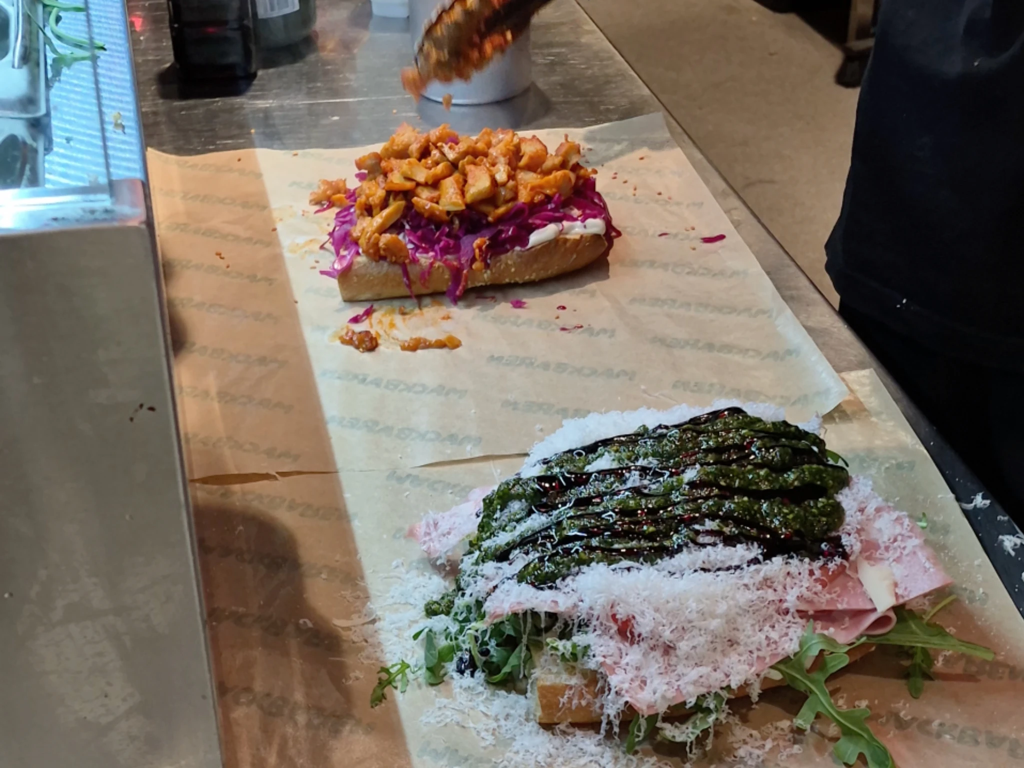 A chef preparing loaded open-faced sandwiches with fresh toppings on branded paper at Mackbaren in Gothenburg.
