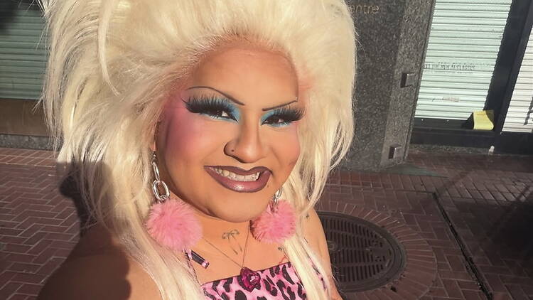 A close-up of a drag performer smiling outside a building A close-up of a drag performer smiling outside a building