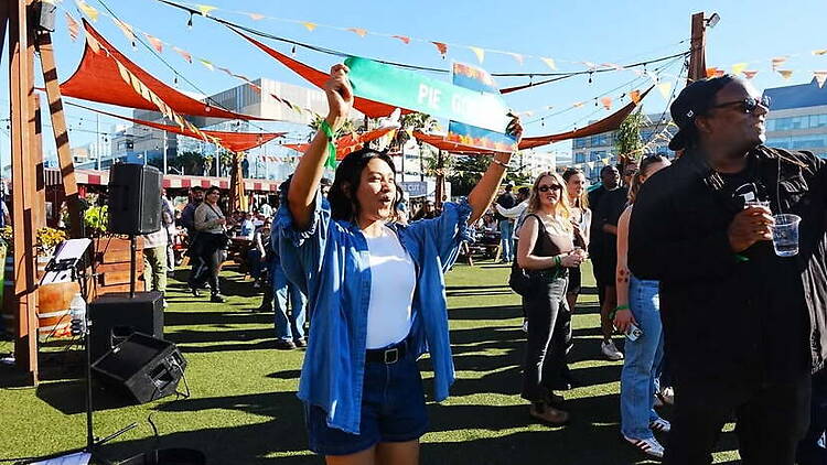 A wide shot of attendees holding a banner and celebrating at an outdoor festival A wide shot of attendees holding a banner and celebrating at an outdoor festival