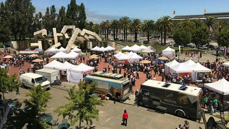A wide shot of people gathering among vendor tents and food trucks at an outdoor festival
