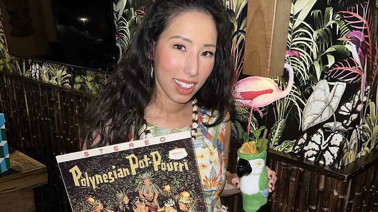 Close-up of a person holding a record and decorative parrot at a tropical-themed venue. Close-up of a person holding a record and decorative parrot at a tropical-themed venue.