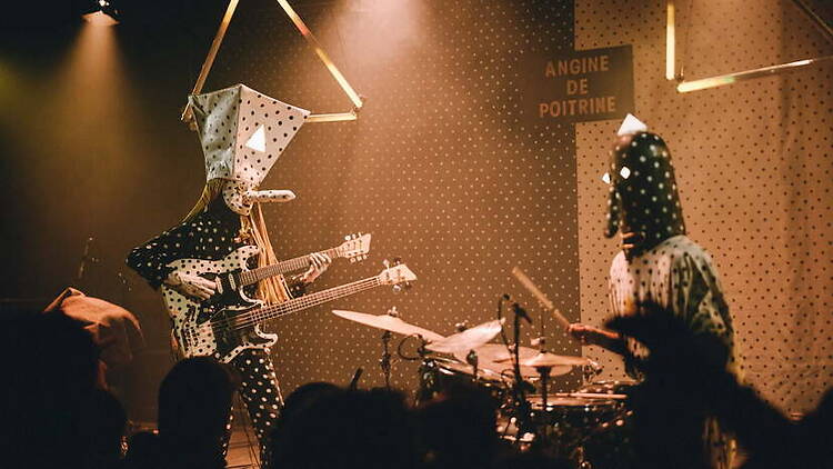 Wide shot of masked musicians performing on stage under warm lighting. Wide shot of masked musicians performing on stage under warm lighting.