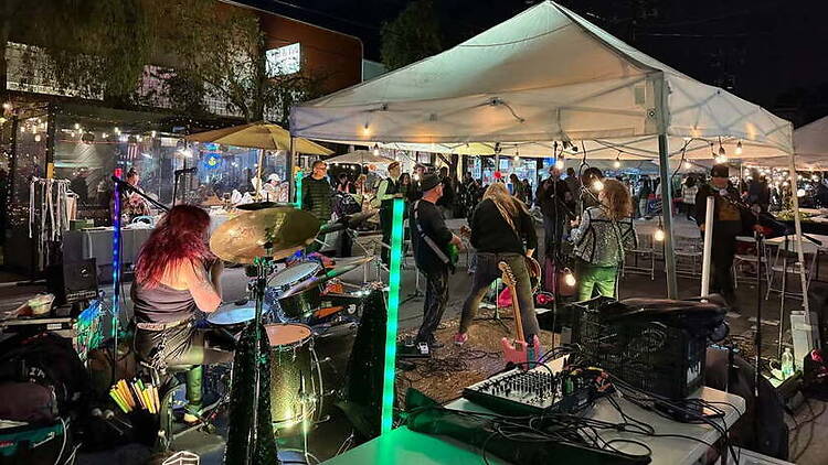 Wide shot of a band performing at a nighttime outdoor market under a tent.