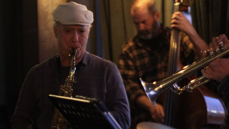 A wide shot of musicians performing jazz with saxophone, trumpet, and double bass on stage.