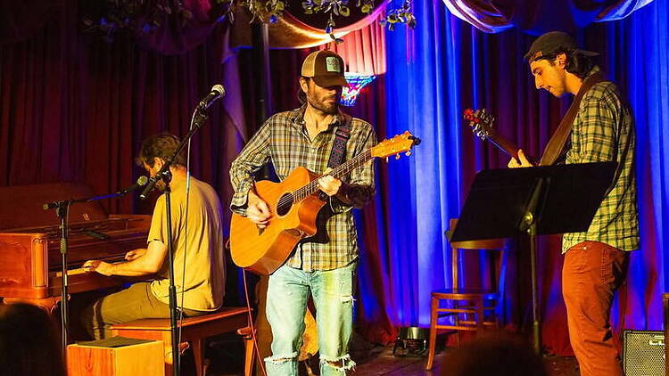 A wide shot of musicians performing with guitars and piano on a stage.