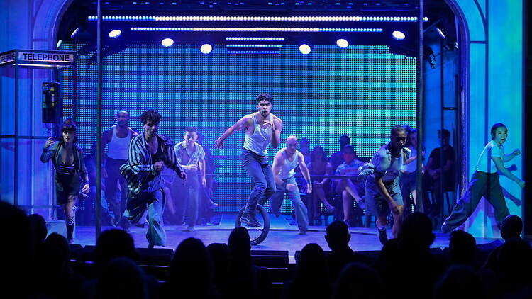 A wide shot of dancers performing on stage before an audience.