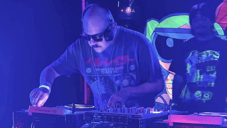 A close-up of a DJ mixing music on a turntable setup under blue stage lights