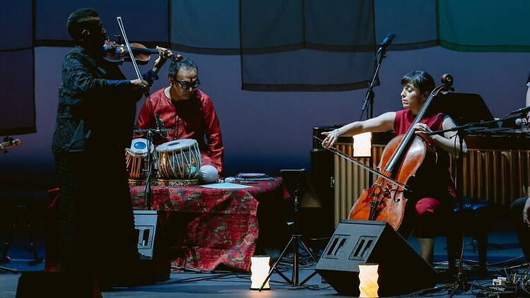 A wide shot of musicians performing with violin, cello, and percussion on stage