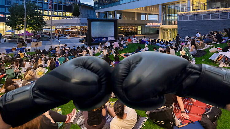 A wide shot of people watching a movie outdoors on a lawn with boxing gloves in the foreground