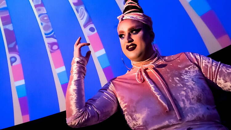 A close-up of a drag performer posing on stage under colorful lights