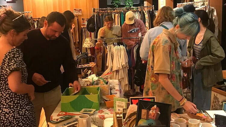 A wide shot of shoppers browsing clothing and handmade goods at an indoor market