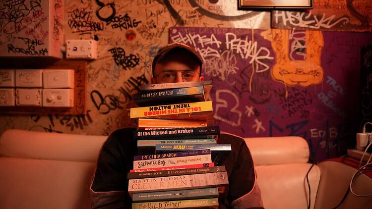 Book Doof Boy holds a pile of books.
