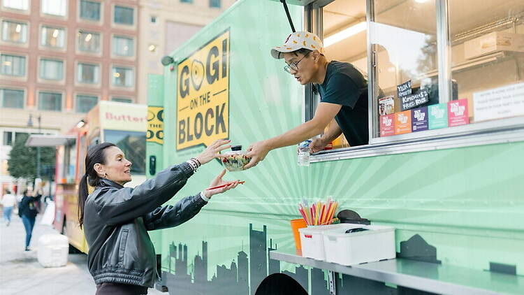 A wide shot of a customer receiving food from a vendor at a food truck