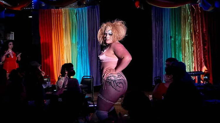 A wide shot of a drag performer posing for an audience on a colorful stage A wide shot of a drag performer posing for an audience on a colorful stage