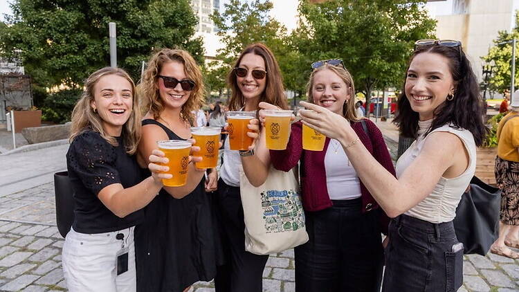 A wide shot of five friends holding drinks together at an outdoor event.