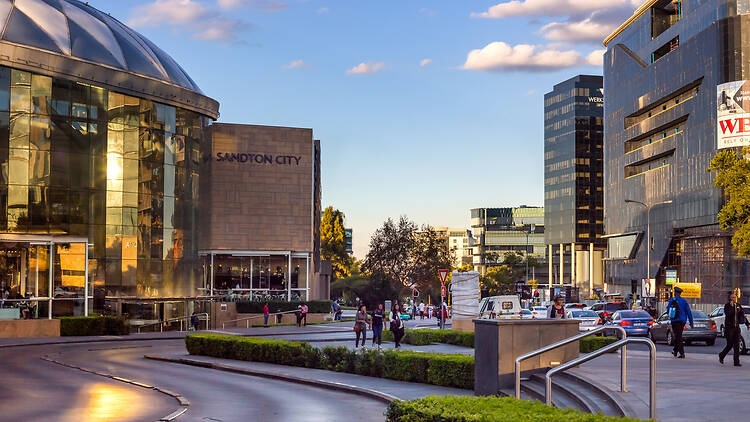 Shopping mall entrance and busy road with pedestrians.