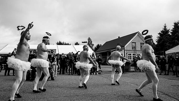 Joukko keski-ikäisiä miehiä pukeutuneine tutuihin tanssimassa ihmisjoukon edessä.