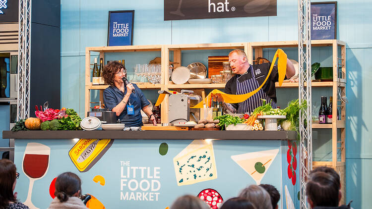 The Little Food Market woman talks while man displayed rolled pasta sheet to an audience