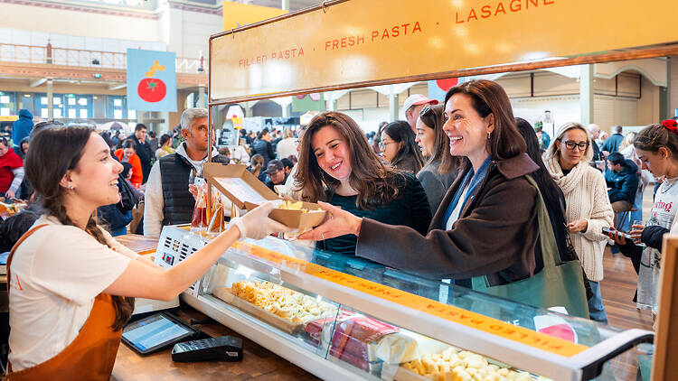The Little Food Market woman serves a box of pasta to two other women