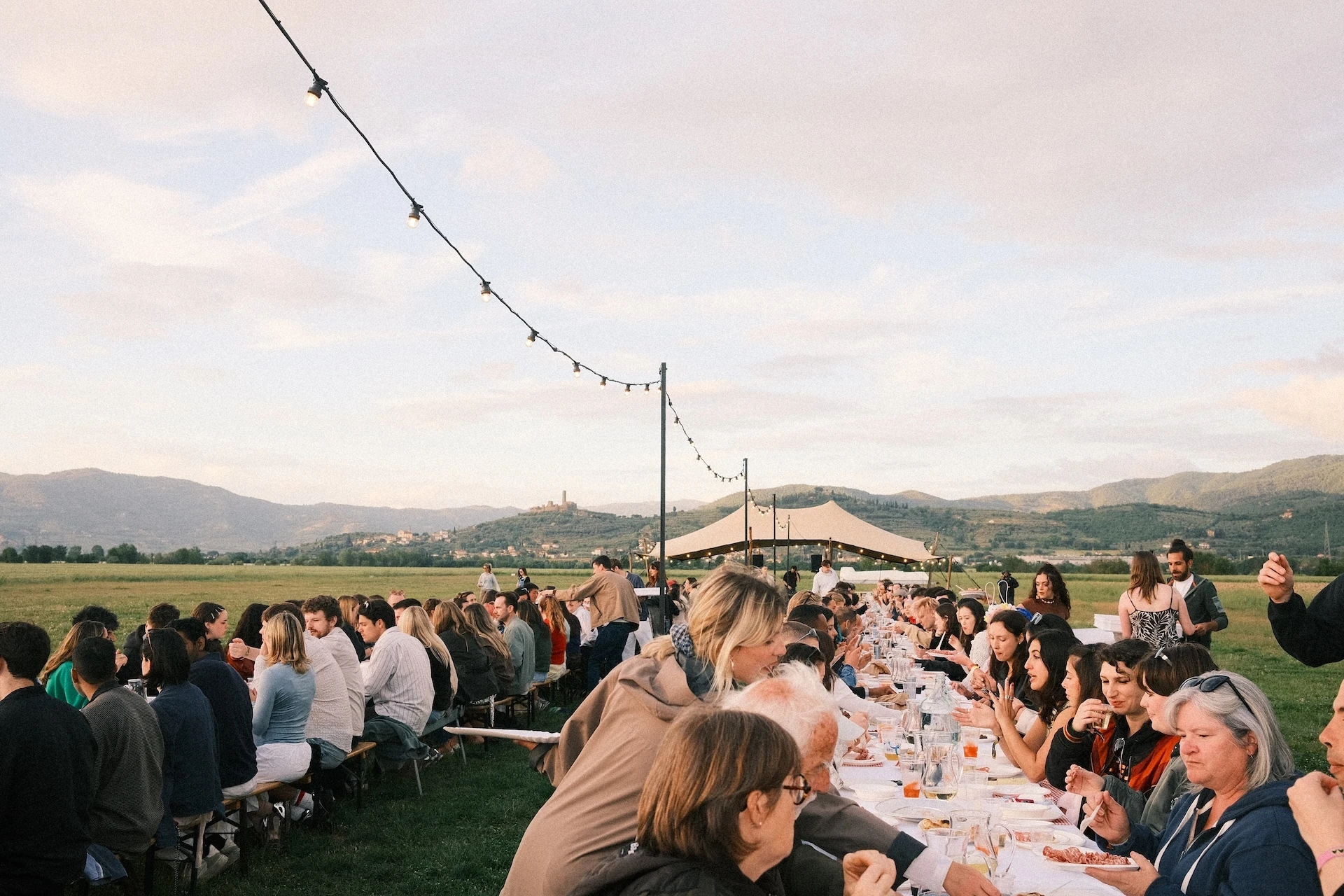 Hundreds of people sit at two long tables at Flash Festival eating and talking