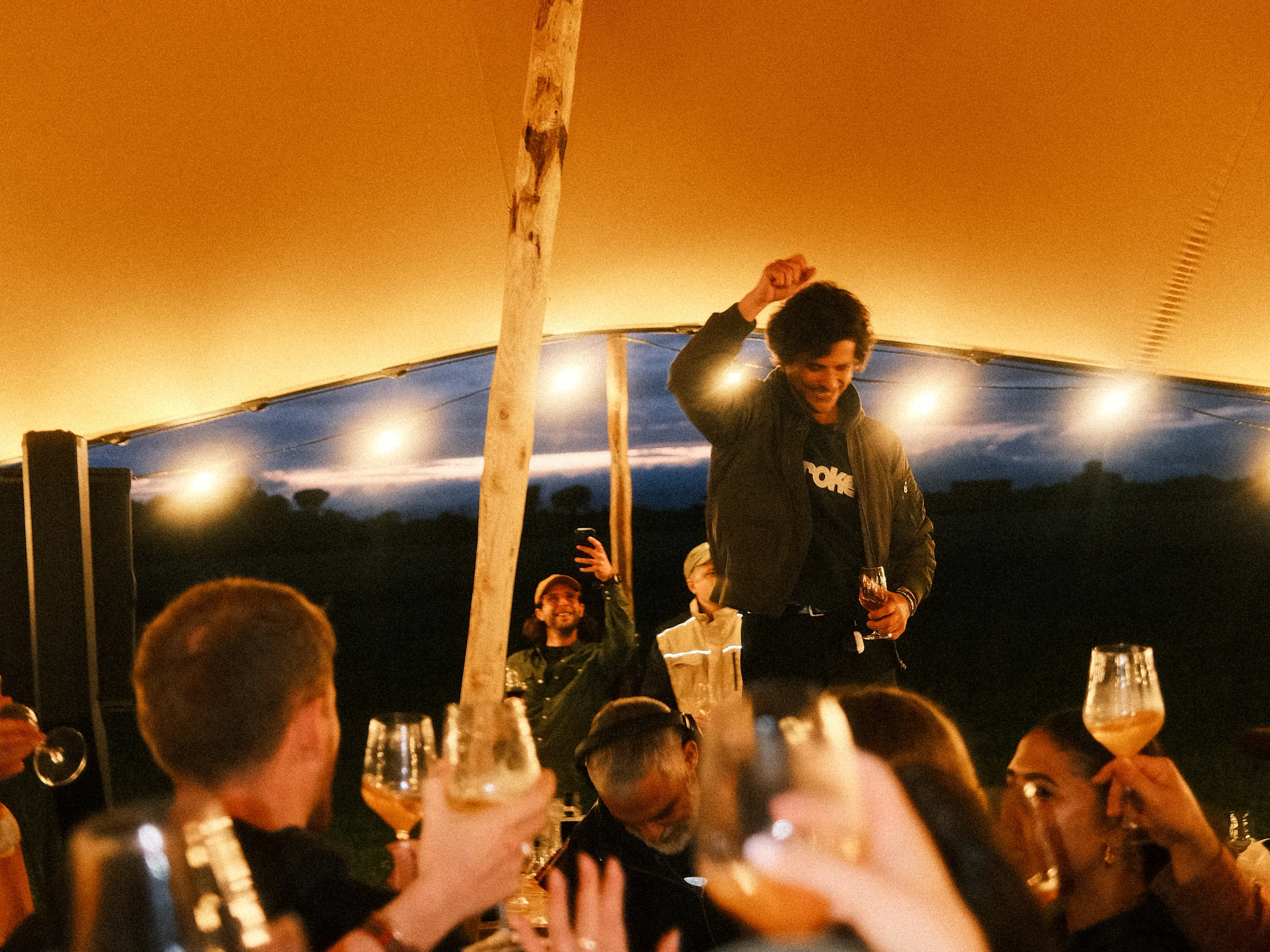 A man dancing in a festival tent while people cheers with wine 