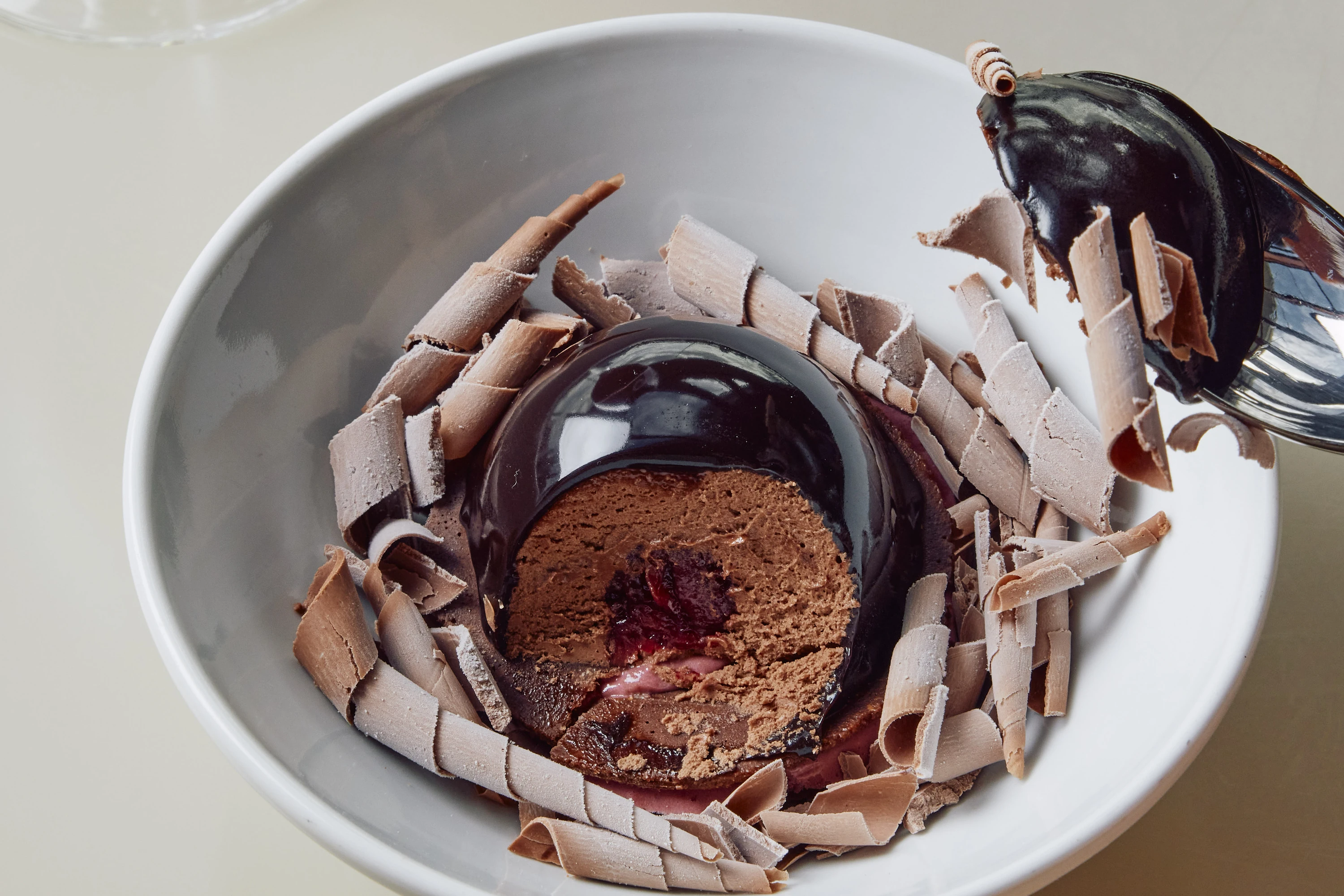 A chocolate half-sphere dessert resembling a shiny cherry, sitting in a bowl of tempered chocolate curls at Bennelong restaurant.