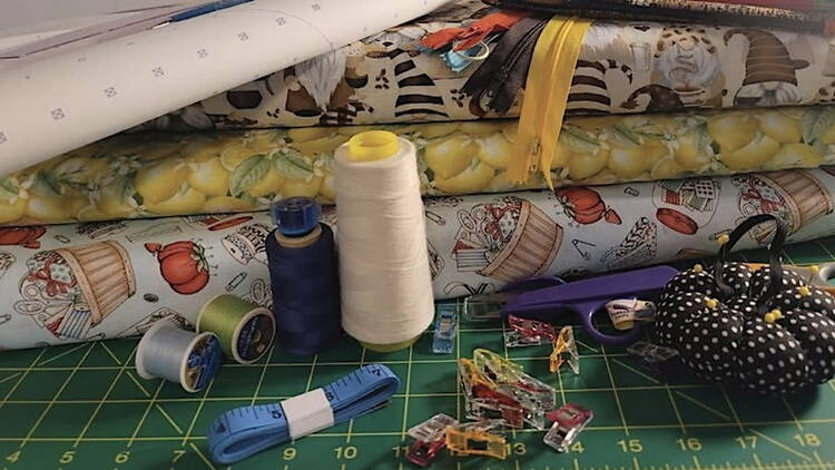A close-up of sewing supplies, fabric, thread, clips, scissors, and a measuring tape on a cutting mat.