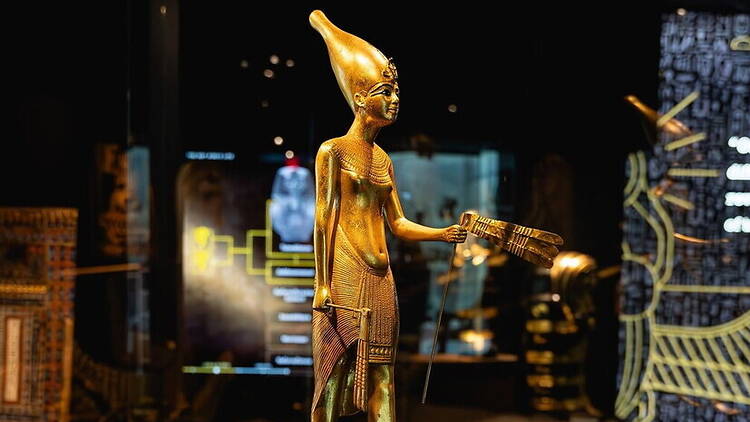 A close-up of a golden Egyptian statue displayed in a museum. A close-up of a golden Egyptian statue displayed in a museum.