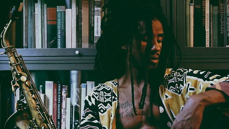 A close-up of a musician sitting beside a saxophone in front of a bookshelf A close-up of a musician sitting beside a saxophone in front of a bookshelf