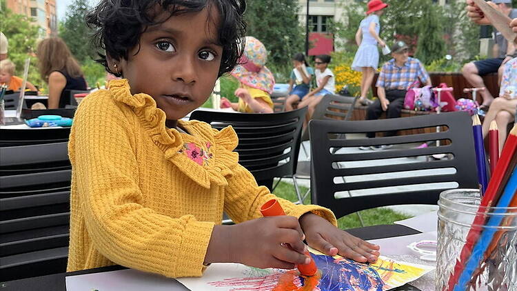 Close-up of a child painting at a table during an outdoor community event. Close-up of a child painting at a table during an outdoor community event.