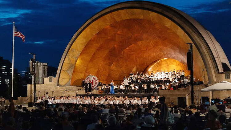 A wide shot of a choir performing onstage at an outdoor amphitheater at night.