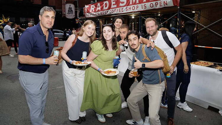 A wide shot of a group posing with food and drinks outside a coffee shop.