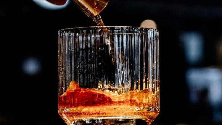 Close-up of amber liquid being poured into a glass on a dark bar counter. Close-up of amber liquid being poured into a glass on a dark bar counter.