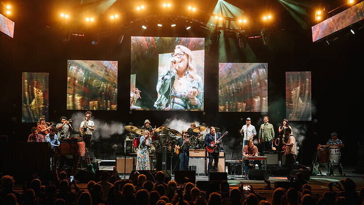 A wide shot of a large band performing on a brightly lit stage before a crowd. A wide shot of a large band performing on a brightly lit stage before a crowd.