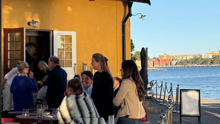 Tapphuset, Skeppsholmen People socializing outside a vibrant yellow waterfront cafe by the water on Skeppsholmen in Stockholm.