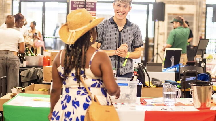 A wide shot of a vendor serving a customer at a market stall indoors. A wide shot of a vendor serving a customer at a market stall indoors.
