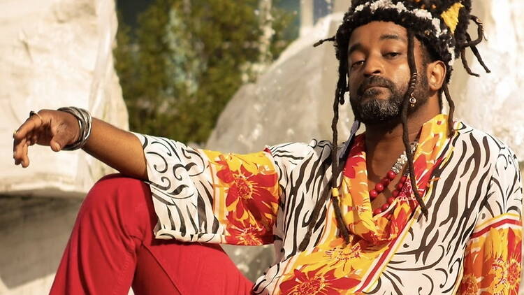 A medium shot of a man posing in colorful patterned clothing outdoors.