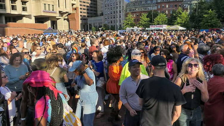 A wide shot of a crowd gathering at an outdoor festival in a city plaza.