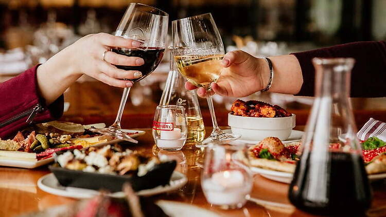 Close-up of hands clinking wine glasses over a dining table in a restaurant Close-up of hands clinking wine glasses over a dining table in a restaurant