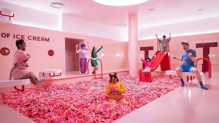A wide shot of people playing and sliding in an indoor pink-themed activity space
